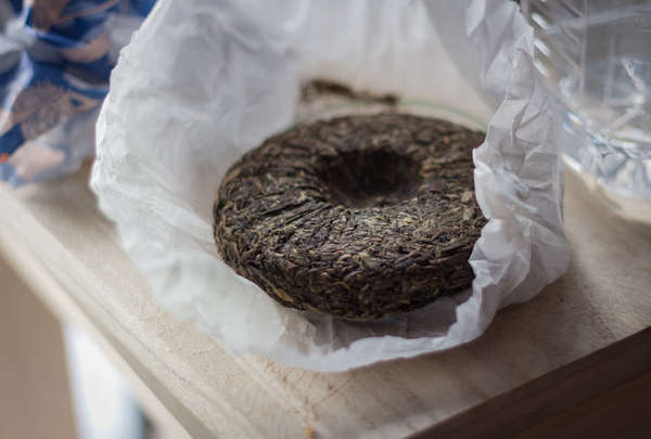 Compressed tea cake, round, with depression in center, unwrapped from white paper, set on a pale wooden table