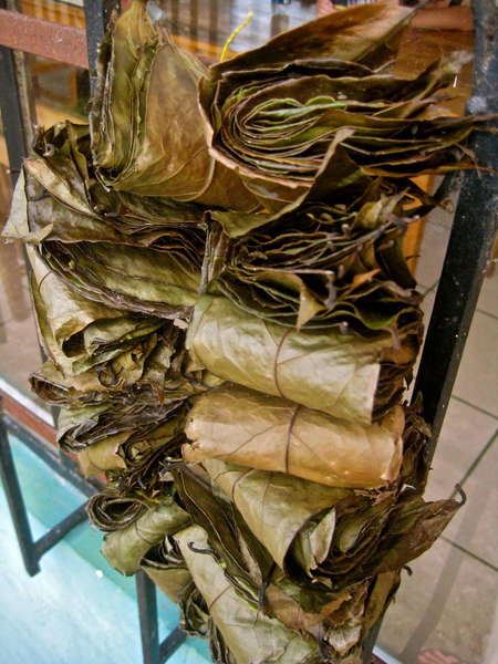 Loosely-tied bundles of massive dried leaves, stacked tall on a shelf