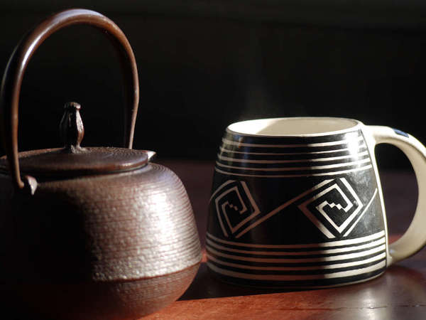 Cast iron teapot on the left, a black-and-white mug widening towards the base, on a brown table against a black background