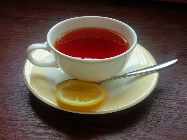 Teacup filled with black tea, lemon slice, and spoon, on saucer