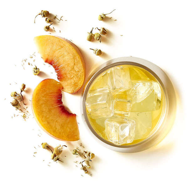 Cup of pale yellow iced herbal tea with ice cubes, two peach slices, and scattered dried chamomile blossoms, on side