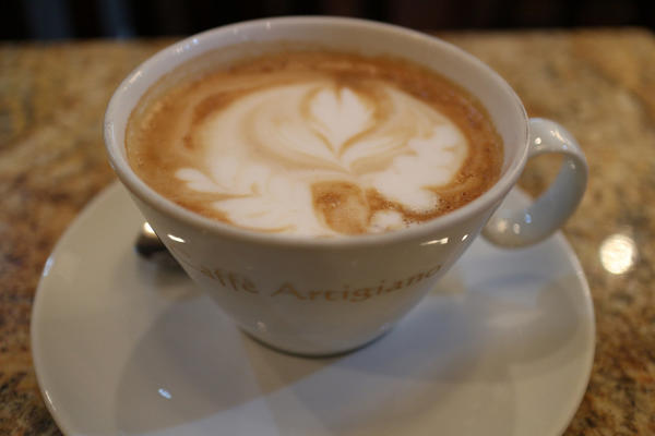 Chai tea latte, with pattern in foam, in teacup reading: Caffe Artigiano