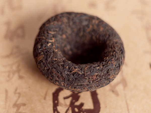 Dark brown tea leaves compressed into a bowl shape, on a paper backgrouund with Chinese characters