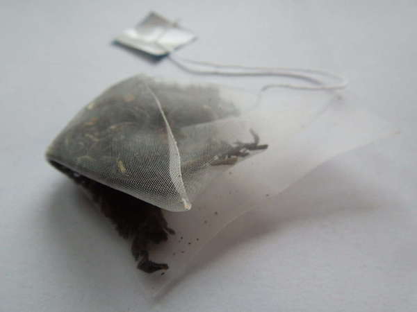 Pyramid-shaped tea bag filled with black tea leaves, attached string and tag, on white background