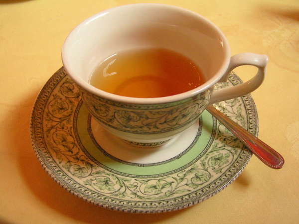 Half-empty cup of tea in ornate teacup with matching saucer, green and white pattern