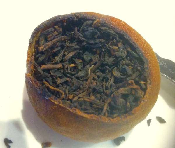 Dark brown tea leaves inside a hollowed-out, dried tangerine