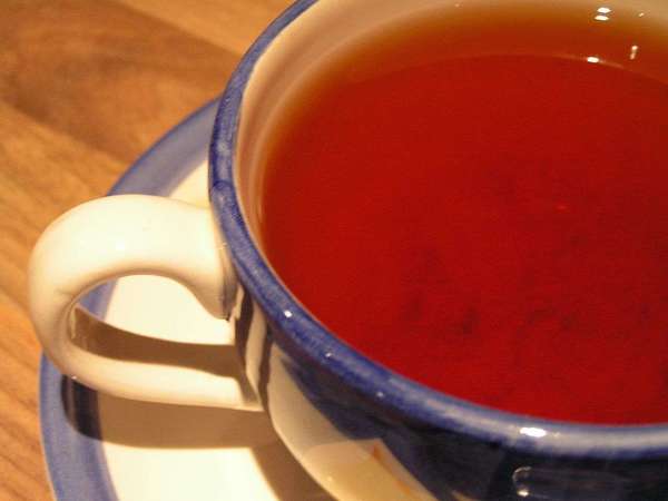 Reddish-colored tea in blue cup with white handle, in white saucer with blue rim, on wooden background