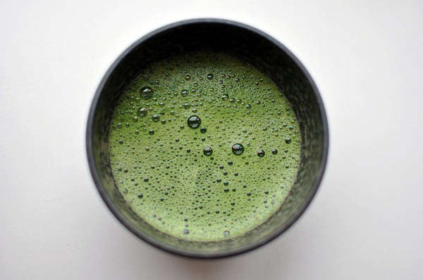 Black bowl filled with bright green liquid with many bubbles and a bit of foam