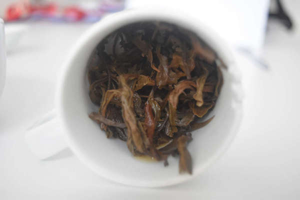 Large, wet, brown tea leaves with crinkly appearance, in white cup after steeping