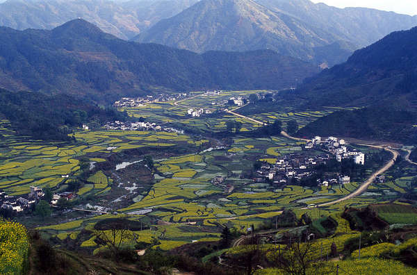 Aerial view of assorted agricultural fields in a river valley, surrounded by mountains, a few scattered buildings about