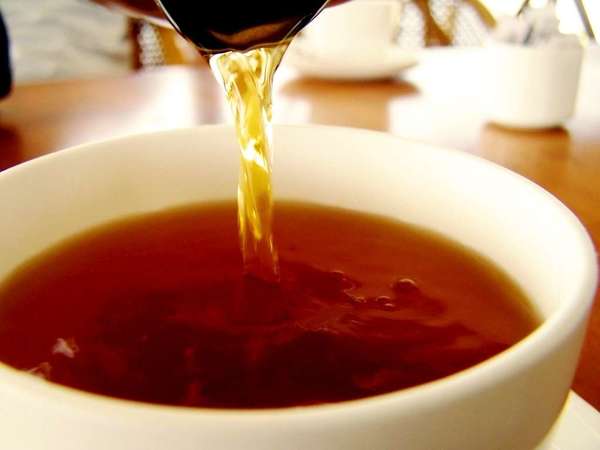 Black tea with a rich reddish-brown color, being poured into a plain white teacup, on a table