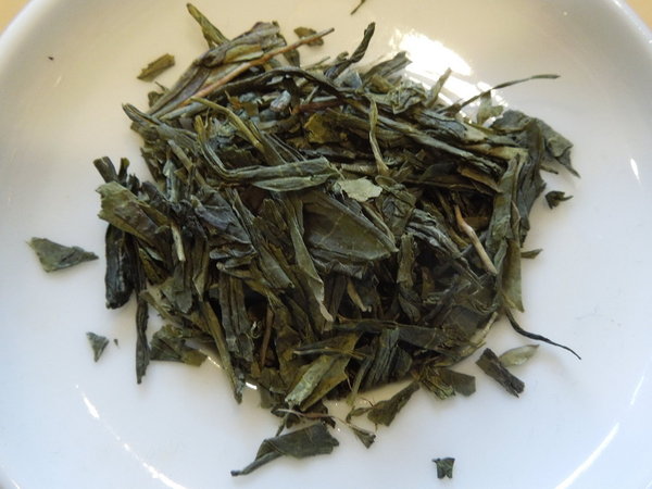Sencha green tea leaves, flat and flakey, in a white dish