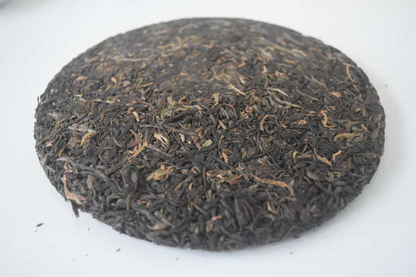 Compressed tea cake, round, mostly dark brown with some orange leaves