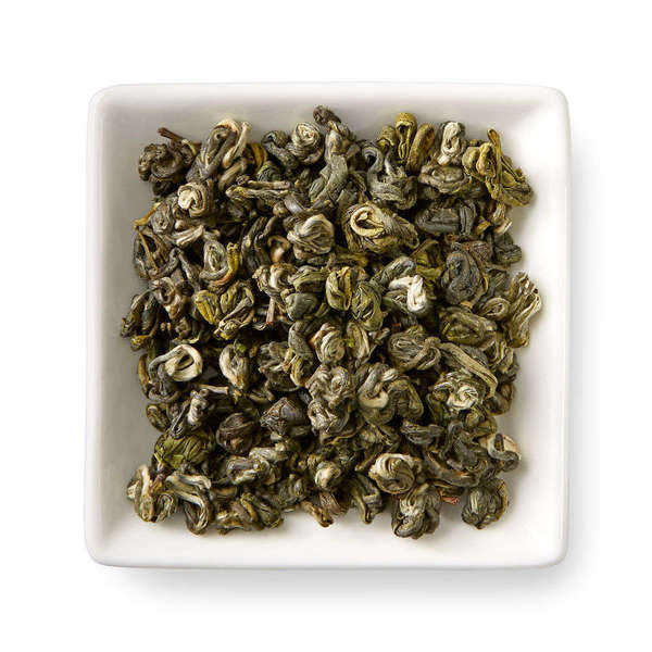 Silvery-golden green tea leaves, tightly rolled into snail shapes, in a square white dish