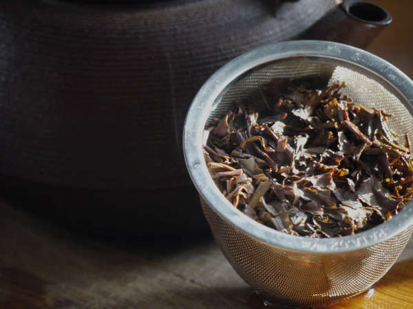 Wet loose-leaf tea in a shiny metal basket, next to a cast iron teapot