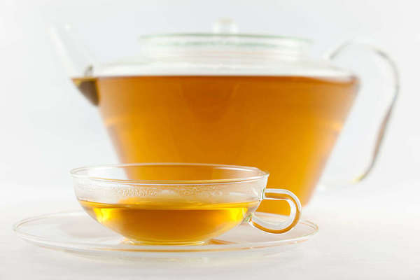 Glass teacup filled with yellow tea liquor, in front of a glass teapot filled with the same white tea