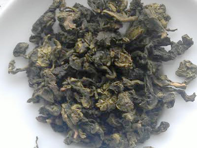 Washed-out green oolong leaves, tightly rolled, in a white dish