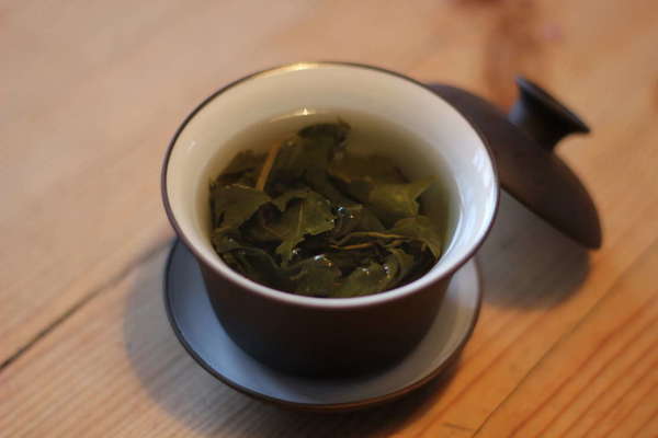 Brown gaiwan with white interior, lid off, containing oolong tea leaves steeping in water