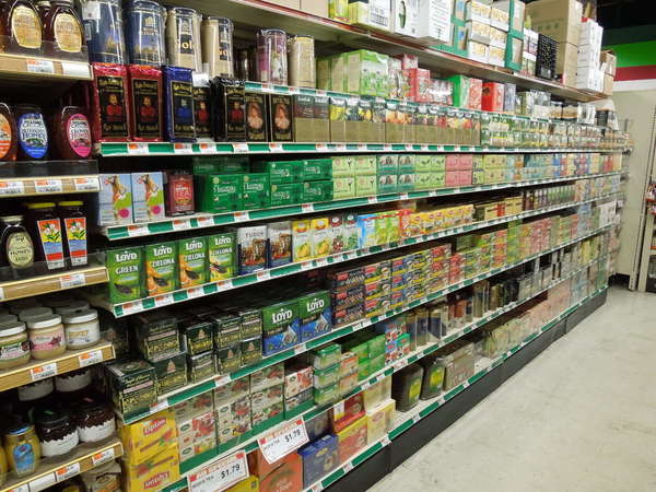 Boxes of tea on the shelf in a supermarket, jars of honey on the left, a few cylindrical containers of tea top